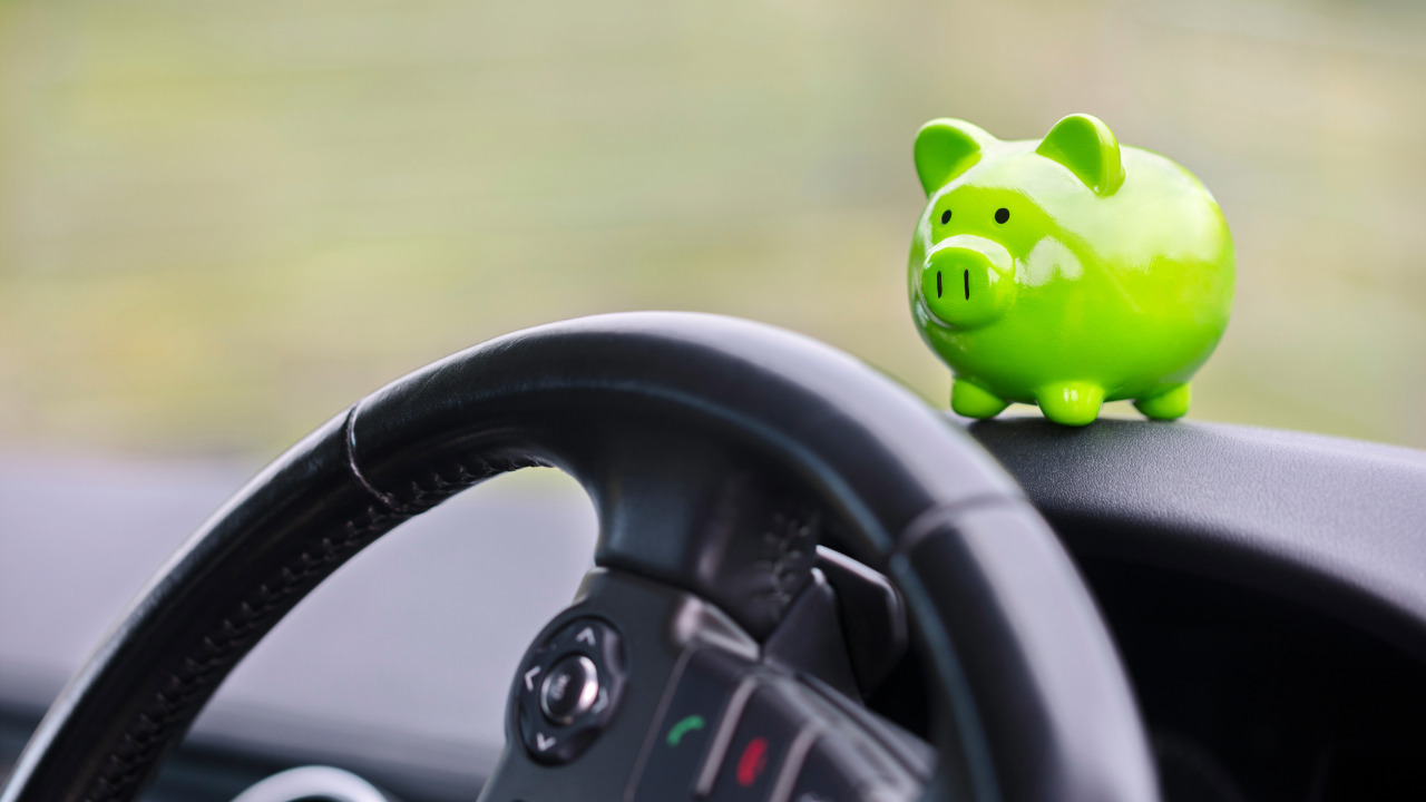 Neue Kilometergeldverordnung hilft Unternehmen beim Steuernsparen gruenes Sparschwein sitzt im Auto Cockpit
