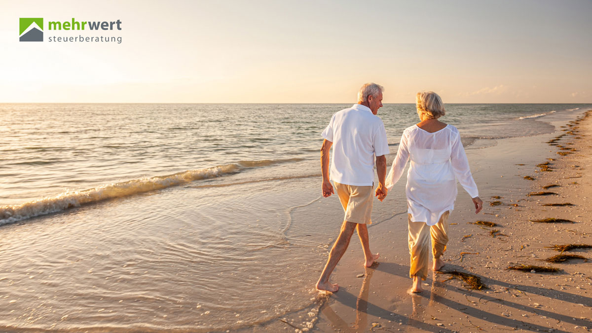 Pensionsvorsorge_Mehrwert-Steuerberatung glueckliches paar hand in hand spaziert am strand bei sonnenaufgang am meer entlang